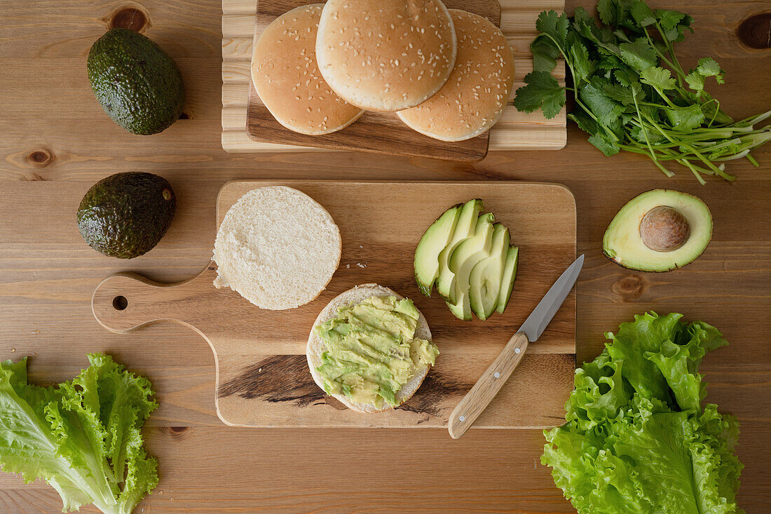 Top view of fresh lettuce vegetable and sliced avocado with burger buns placed on cutting board over wooden table