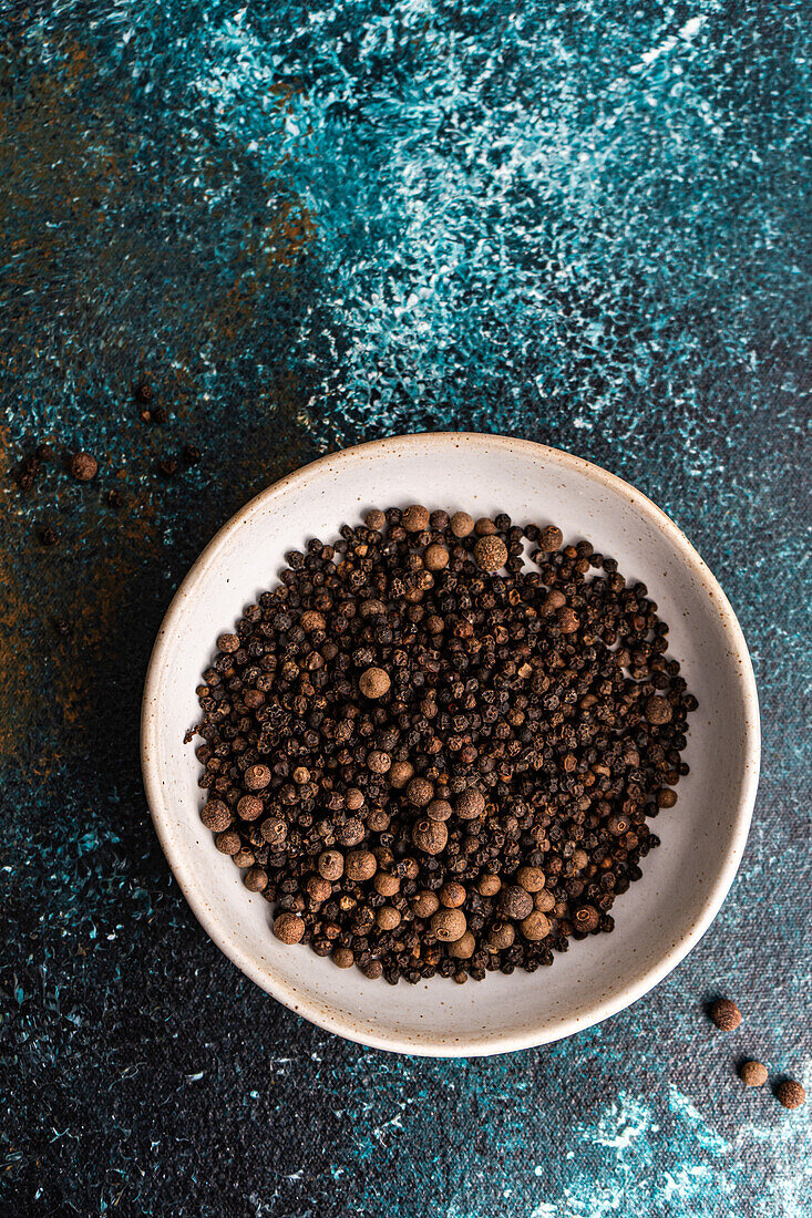 Top view of bowl filled with natural aromatic Black pepper in grain on blue concrete background