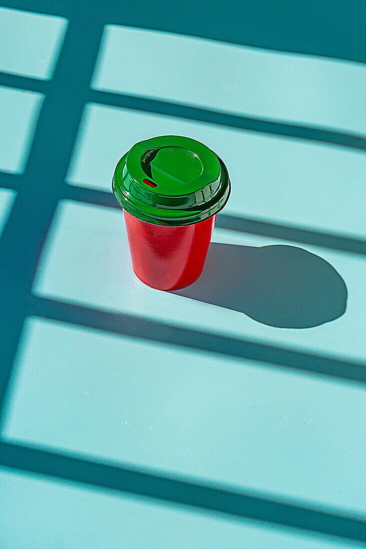 Minimalistischer roter Plastikbecher mit Kaffee zum Mitnehmen und grünem Deckel vor blauem Hintergrund, von oben gesehen