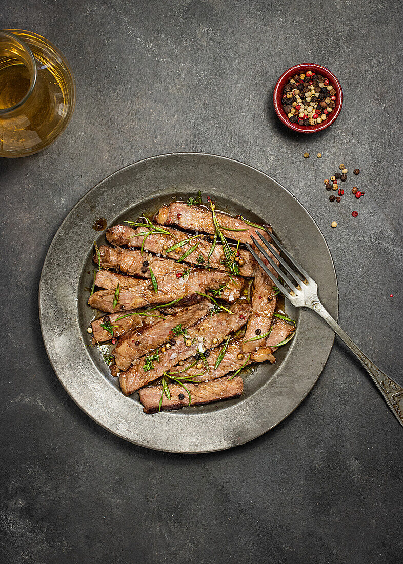 From above delicious sliced roast beef tagliatta served on plate near bowl with herbs placed on concrete table background