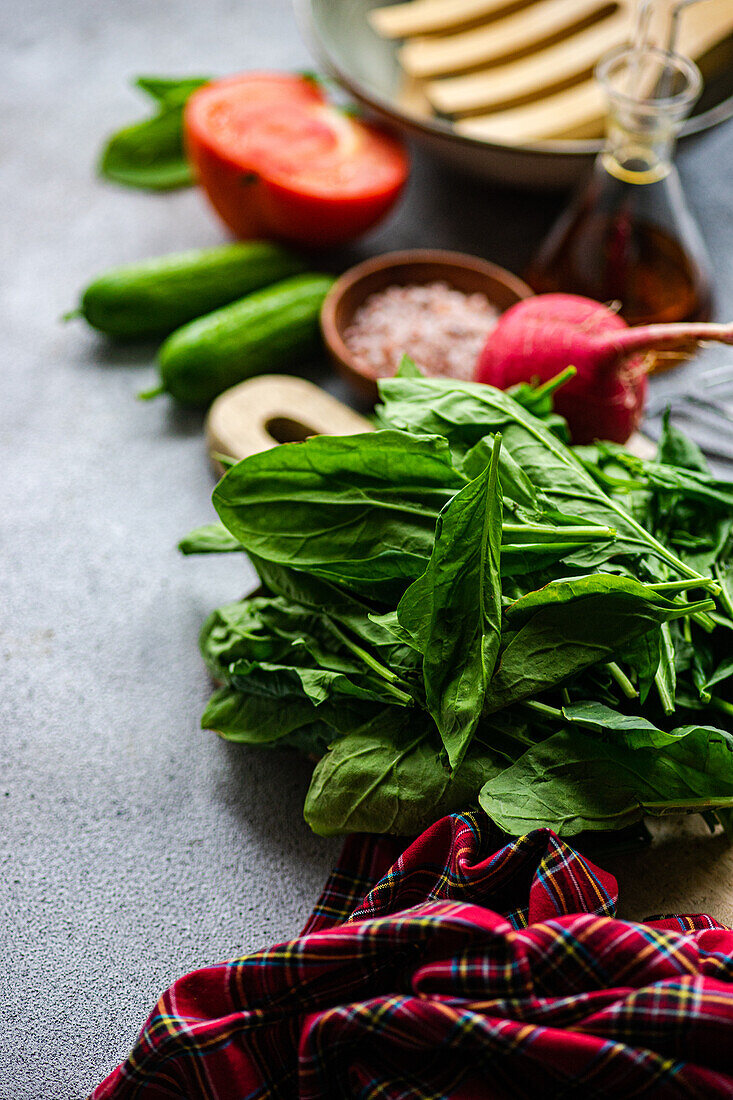 Lush spinach leaves forefront on a table with sliced tomatoes, zucchini, and a bowl of spices, all prepped for a nutritious salad creation