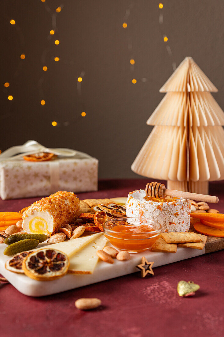 Eine Gourmet-Käseauswahl mit Honig, Crackern und Trockenfrüchten vor einer Kulisse aus glitzernden Lichtern und einem Papierweihnachtsbaum