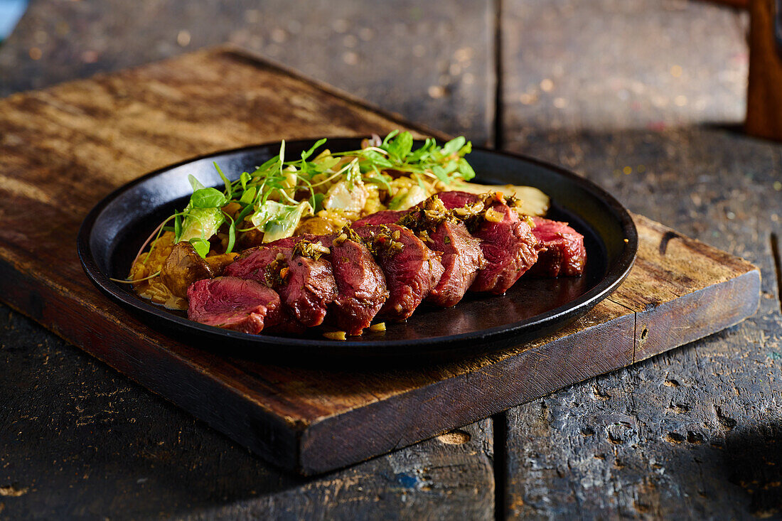 High angle of appetizing traditional Ecuadorian dish made of roasted meat with sauce herbs and vegetables served on black plate on cutting board