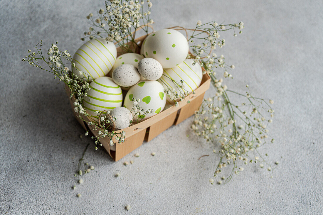 Eine charmante Sammlung von bemalten Ostereiern mit Streifen und Punkten verziert, in einem Korb mit zarten Frühlingsblumen eingebettet