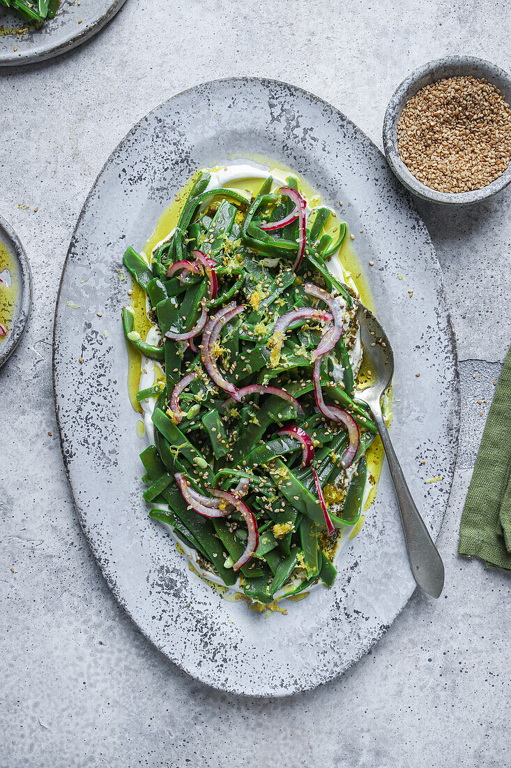 Top view of appetizing vegetarian salad with green herbs and onion slices served on plate with oil and garnished with lemon peel on table