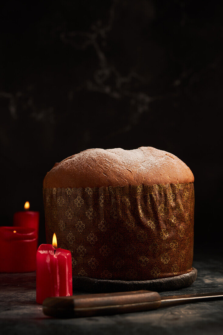 A beautifully presented panettone with a rustic backdrop, illuminated by the warm glow of red candles.
