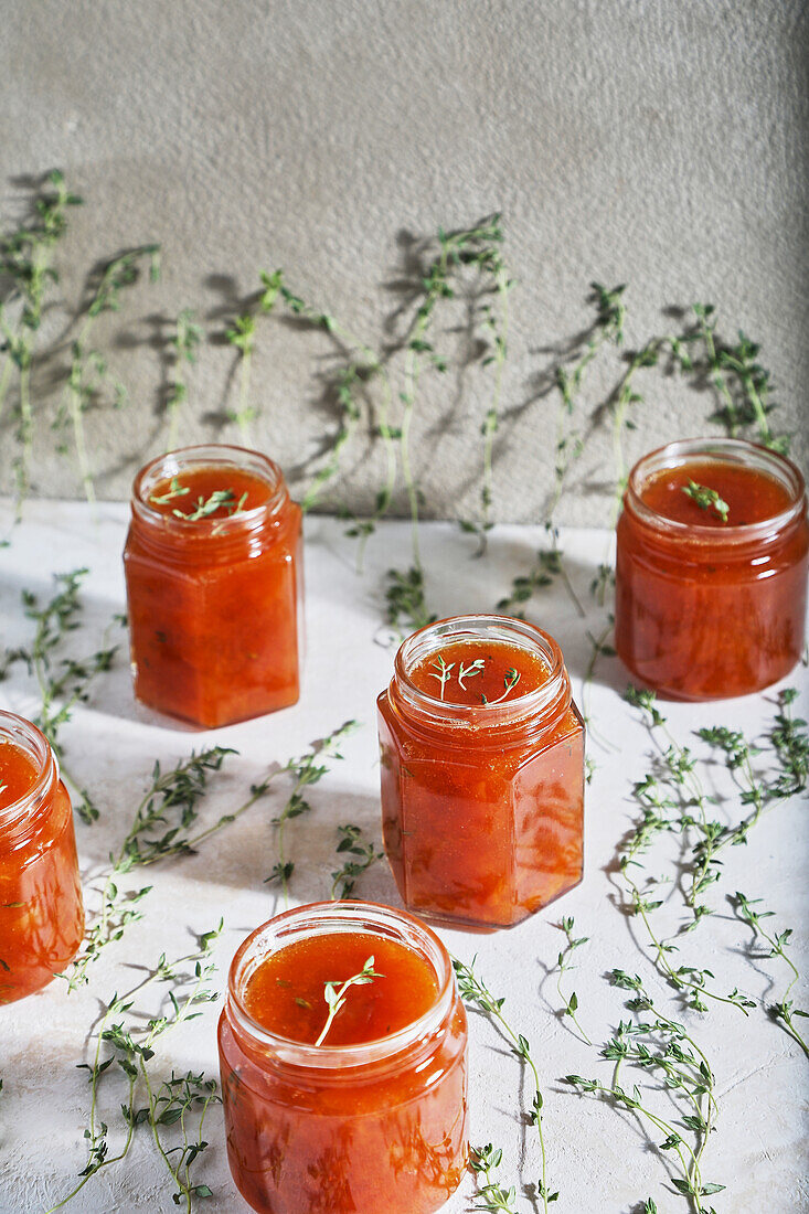 Jars filled with homemade fruit jam placed on table with green sprigs of thyme