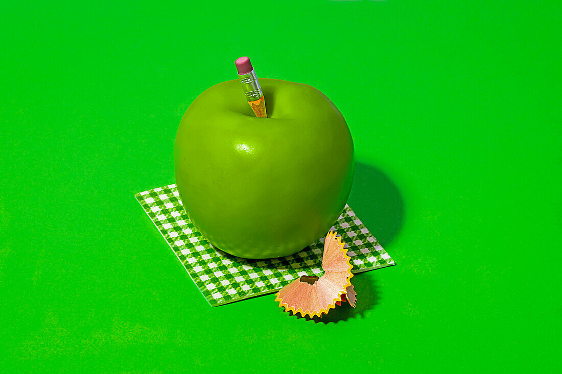 Pencil on healthy Granny Smith apple placed on check pattern cloth near pencil shavings on bright green background