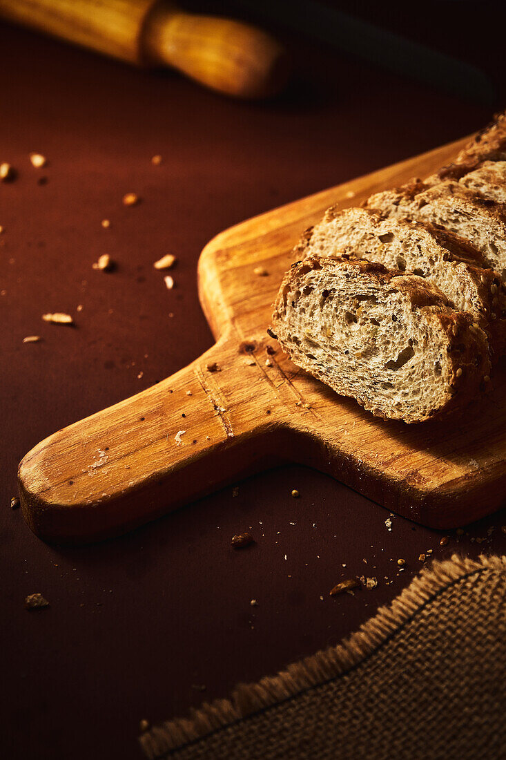 High angle of delicious freshly baked bread with crispy crust sprinkled with mix of seeds and placed on wooden cutting board