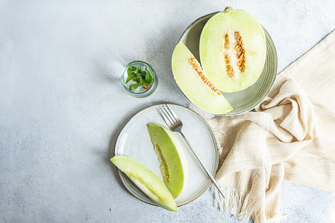 From above of green melon split in half placed in bowl and on plate with a lemonade on a concrete background