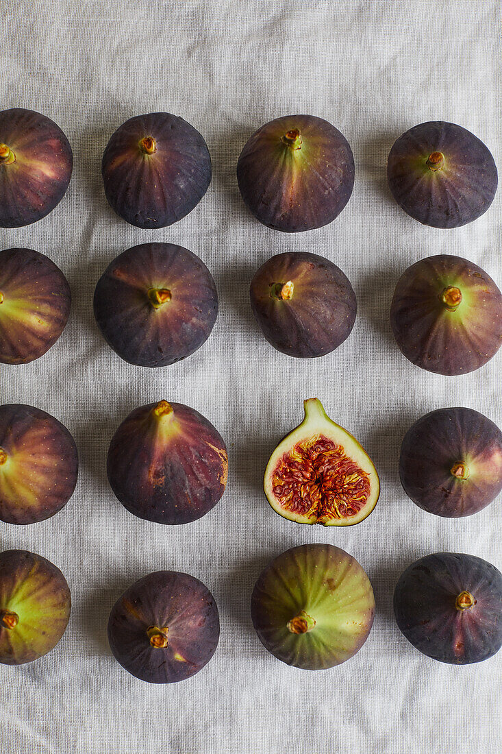 Top view of minimalist composition with half sweet fig placed on gray napkin surrounded by rows of fresh figs