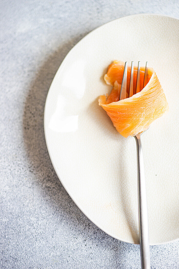 Top view of healthy salmon rolled on fork served on white plate against gray surface