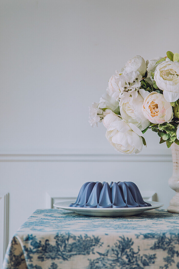 Süßes veganes blaues Panna-Cotta-Dessert auf einem Teller, der auf dem Tisch neben Blumen steht