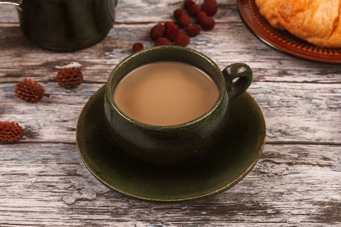 A cup of creamy coffee on a rustic wooden table with snacks.