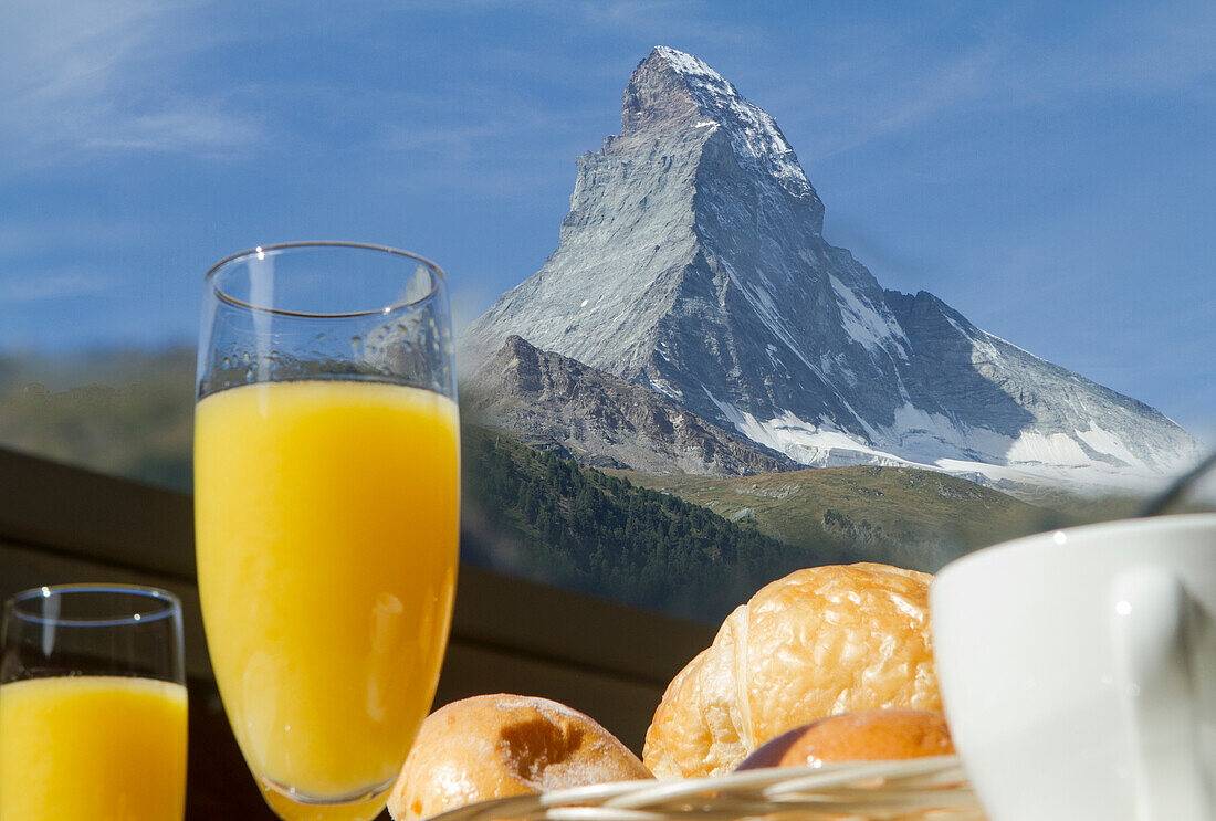 A refreshing morning scene with a glass of orange juice and pastries set against the majestic backdrop of the Matterhorn peak under a clear blue sky