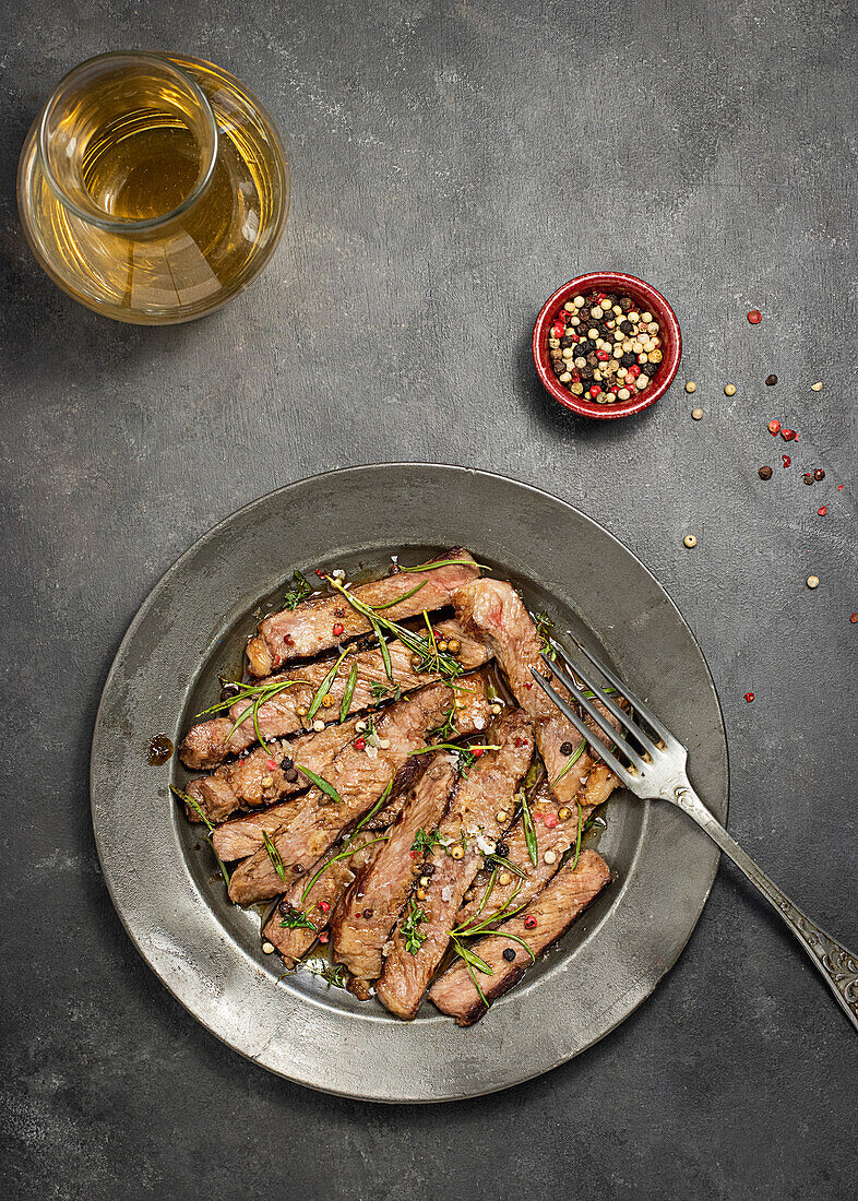 Von oben köstliche Roastbeef-Tagliatta auf einem Teller neben einer Schüssel mit Kräutern auf einem Betontisch serviert