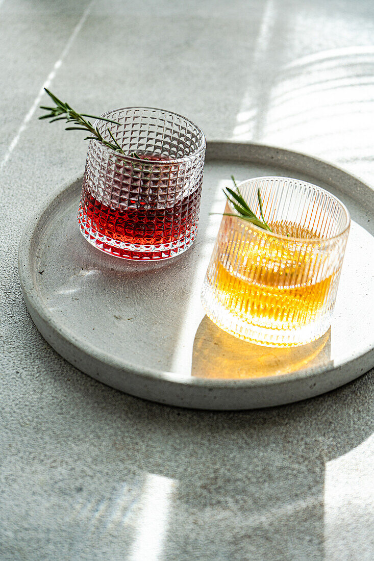 Handwerklich hergestellte Cocktails mit Wodka, Kirsche und Apfelsaft in mit Rosmarin verzierten Gläsern auf einer schattigen Betonfläche von oben