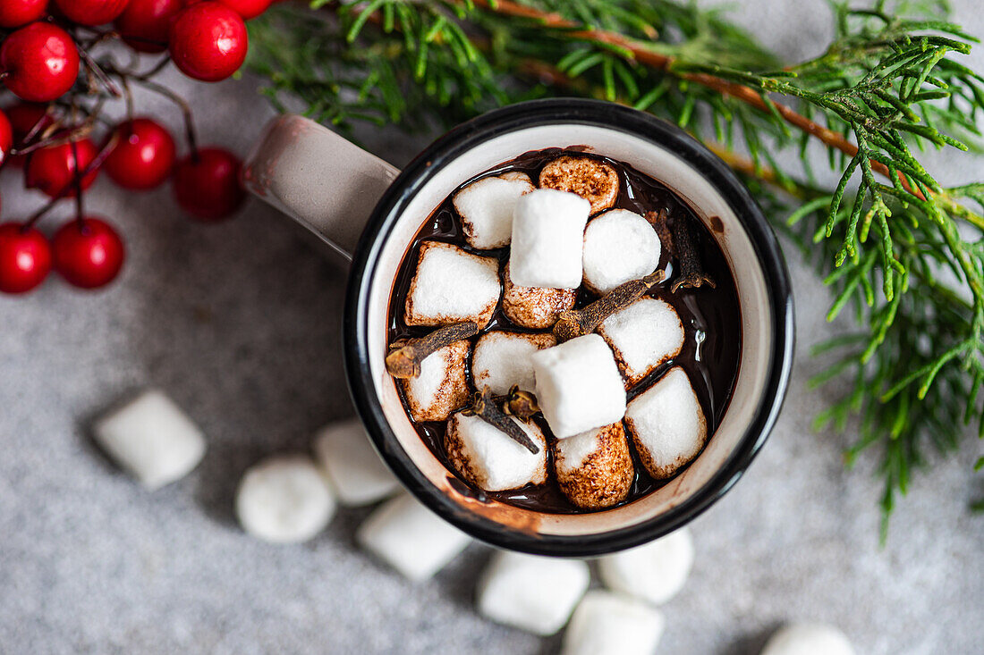 Top view of mug of cocoa with marshmallow near fir twigs on gray background in Christmas time