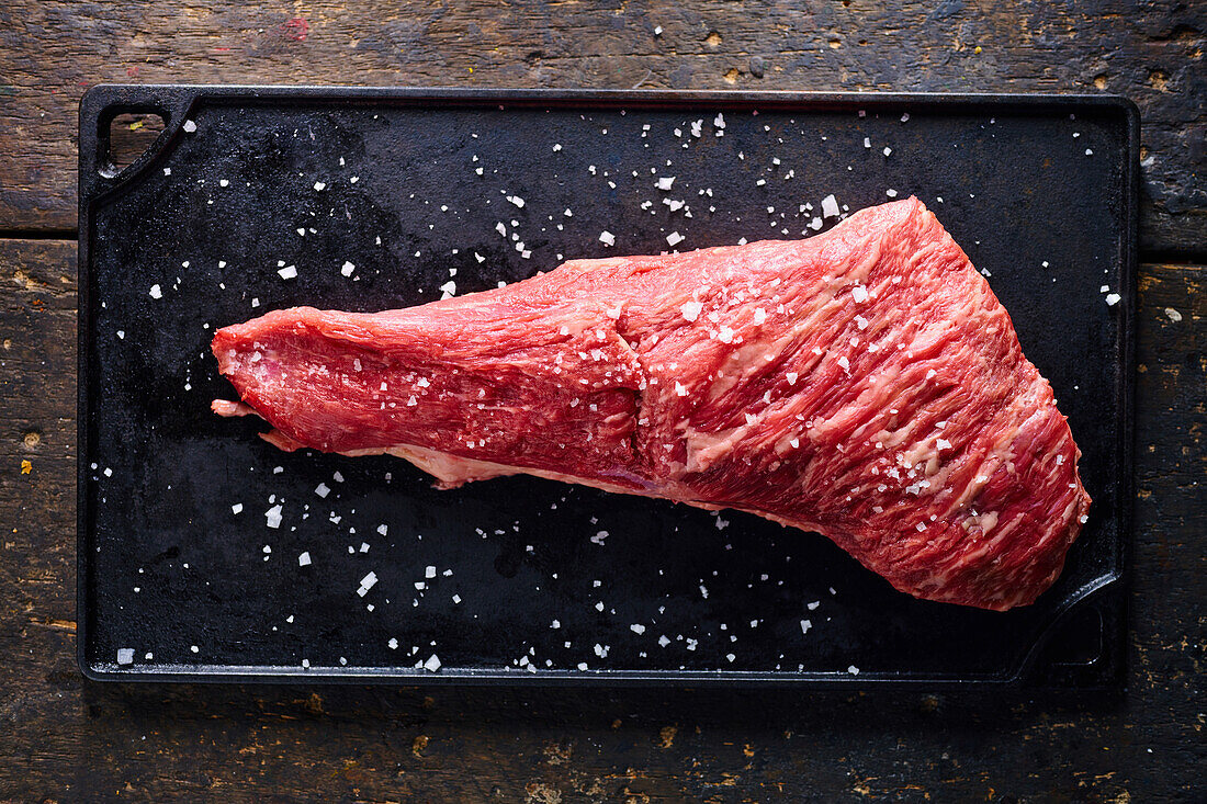 Top view of raw meat piece placed on black tray sprinkled with salt for cooking traditional Ecuadorian dish