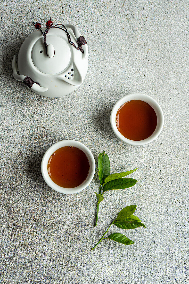 Top view of tea set in Asian style with lemon leaves placed on gray surface