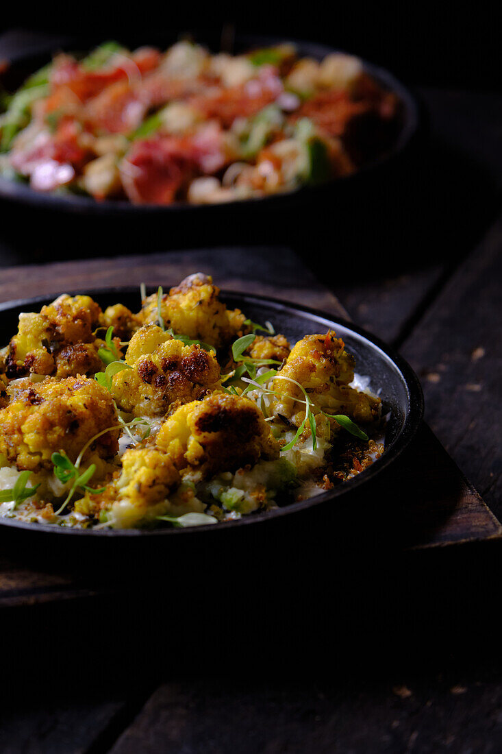 High angle of traditional Ecuadorian roasted cauliflower garnished with herbs served on black plate against blurred background