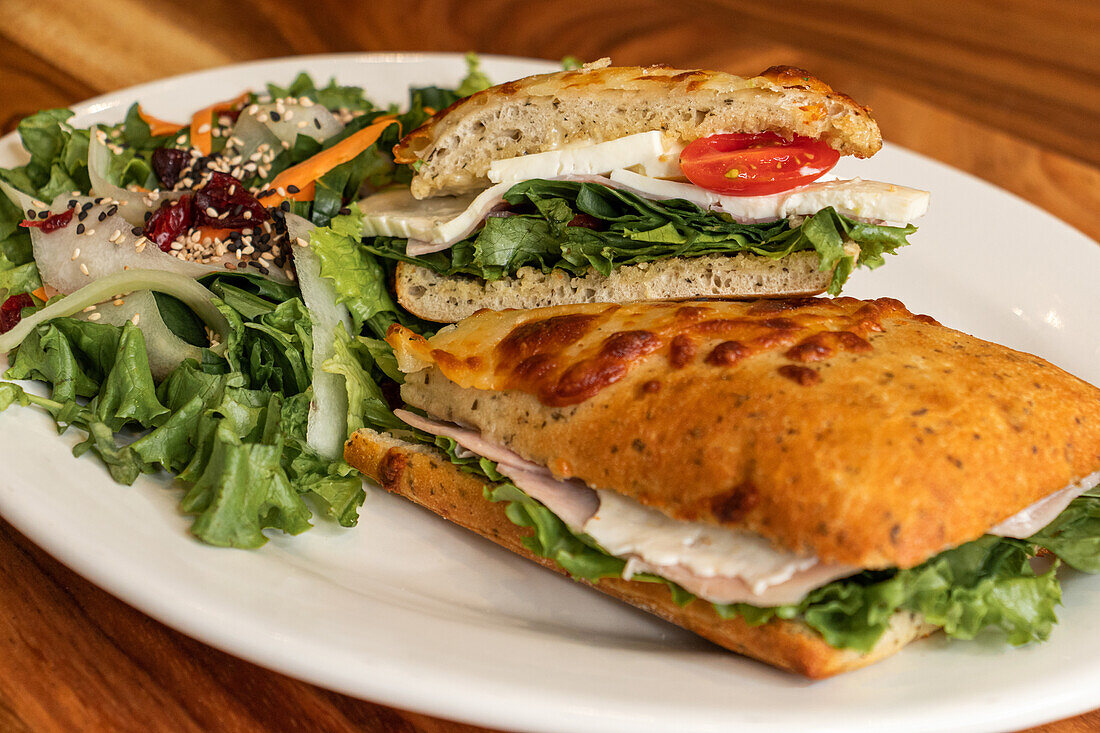 Blick von oben auf ein appetitliches Sandwich mit geschnittenen Tomaten und Salat, serviert auf einem weißen Marmorteller auf einem Holztisch mit gebratenen Chapatas mit Käse im Tageslicht