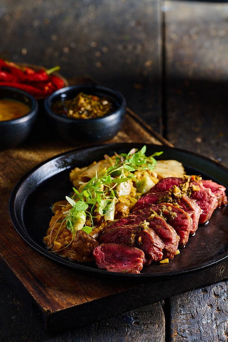 High angle of appetizing traditional Ecuadorian dish made of roasted meat with sauce herbs and vegetables served on black plate on cutting board