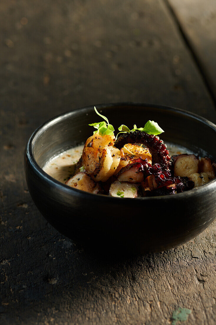 High angle of appetizing traditional Ecuadorian seafood consisting of grilled shrimps and octopus tentacle garnished with herbs and sauce in bowl