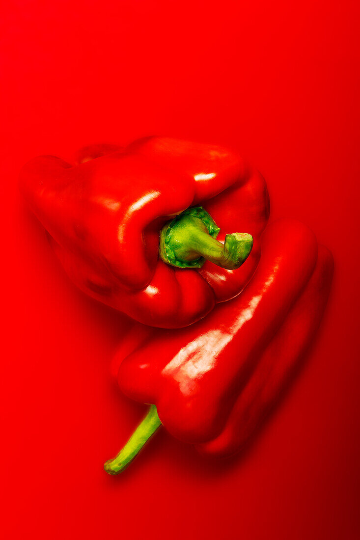 Top view of ripe red peppers placed on top of each other against red background