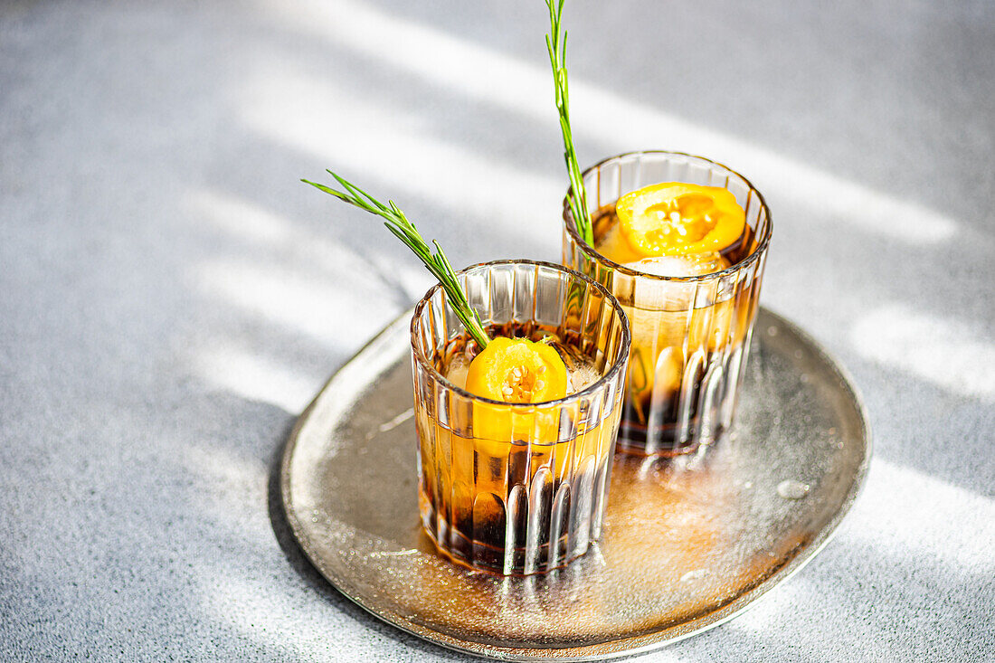 Schrägansicht eines würzigen Margarita-Cocktails mit Eiswürfeln und frischen Fruchtscheiben auf einem Tablett vor grauem Hintergrund