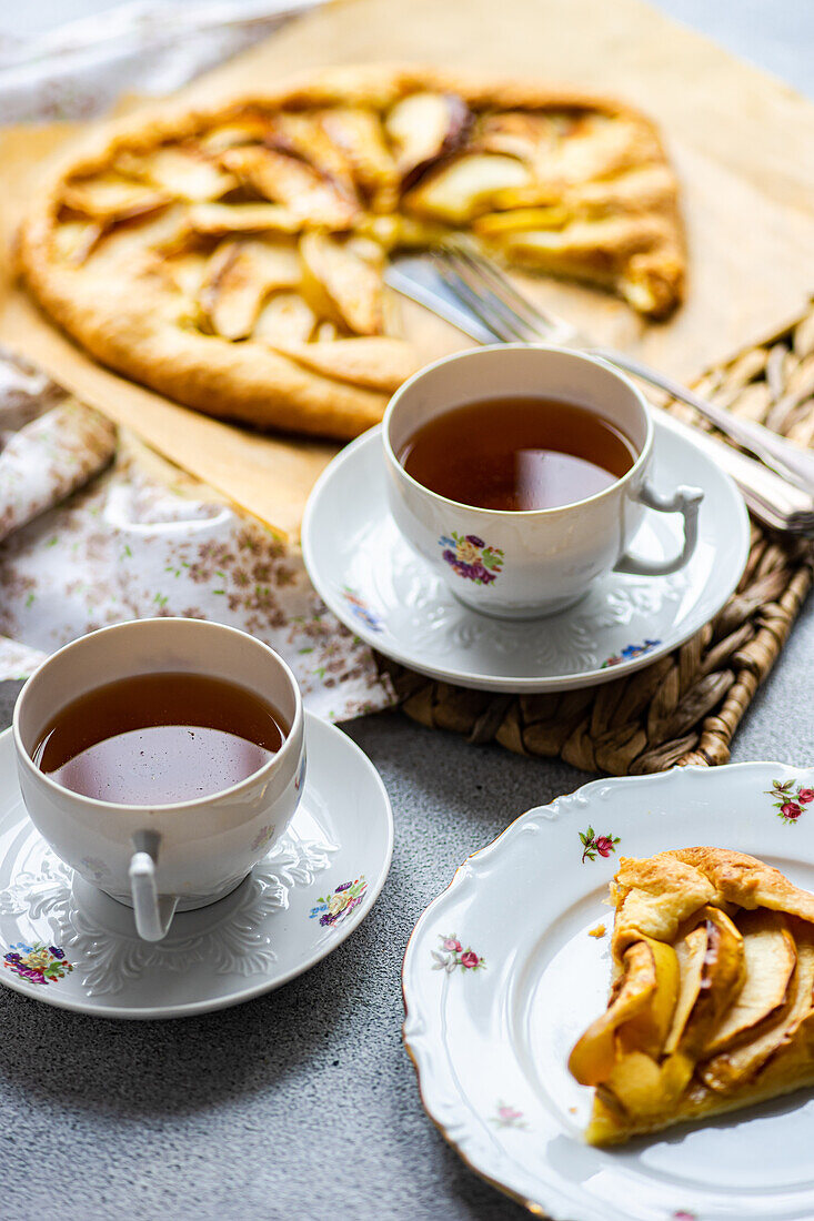Hoher Winkel von Tellern mit Stücken von Apfelkuchen und Tassen mit Tee, serviert auf einem rustikalen Tablett auf einem grauen Tisch