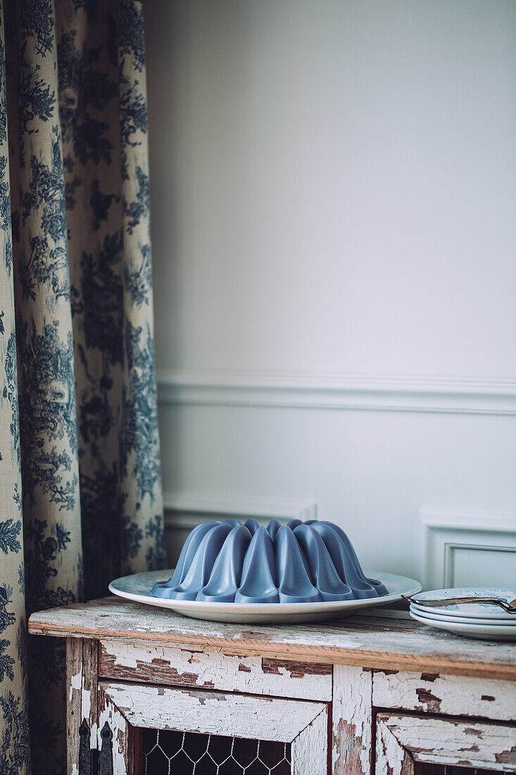 Sweet vegan blue panna cotta dessert on plate placed on vintage wooden cabinet near curtain