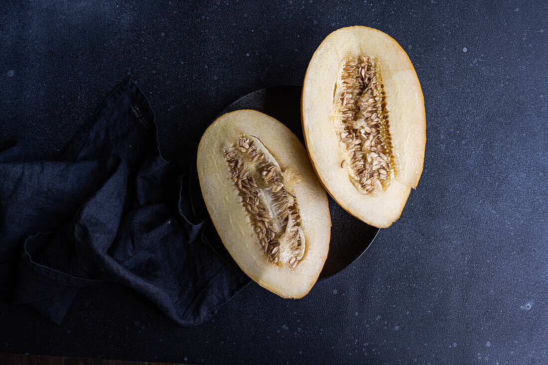Draufsicht auf Scheiben von süßer, gerissener Melone, serviert in einem Keramikteller auf einem schwarzen Betontisch