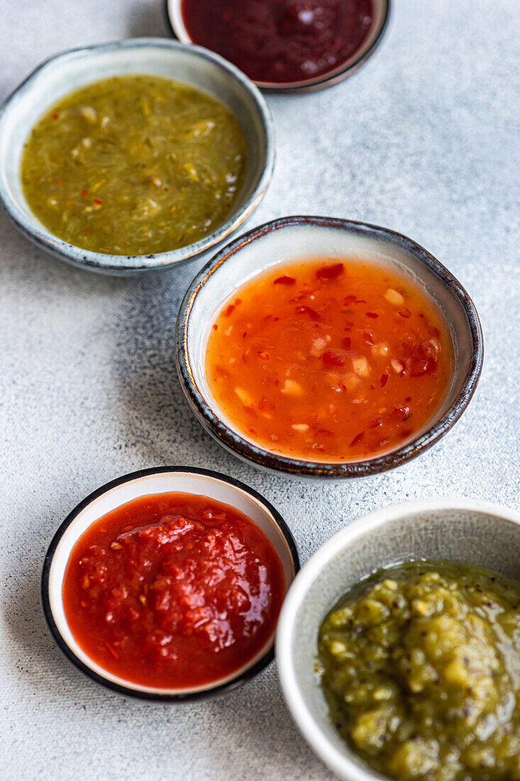 High angle of bowls with traditional Georgian sauces : green plum Tkemali sauce, tomato and cilantro Satsebeli sauce and Kiwi satsebeli placed on white surface