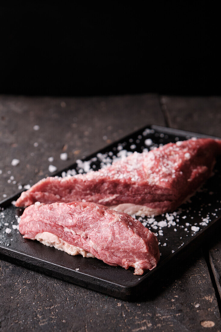 From above of raw meat pieces placed on black tray sprinkled with salt for cooking traditional Ecuadorian dish