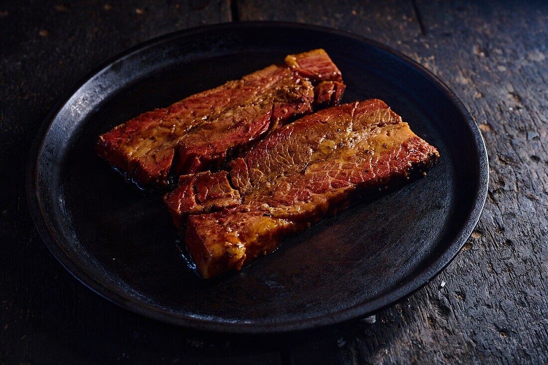 High angle of appetizing fat grilled pork ribs served on black plate placed on wooden table against blurred background