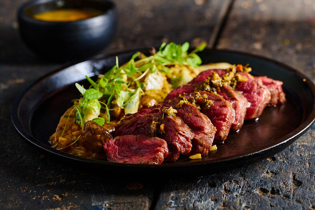 High angle of appetizing traditional Ecuadorian dish made of roasted meat with sauce herbs and vegetables served on black plate on wooden table