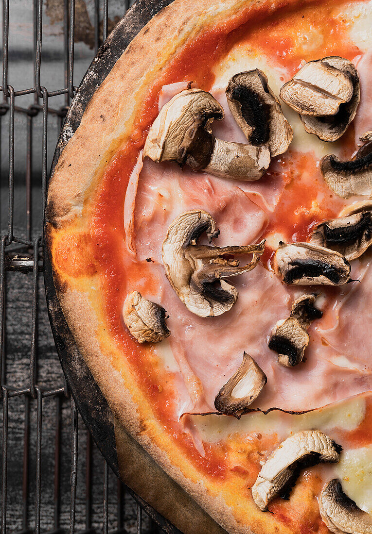 Top view of crop appetizing homemade delicious yummy baked pizza with cheese sliced mushrooms onion pieces tomatoes and sauce placed on frying pan on metal grid in daylight