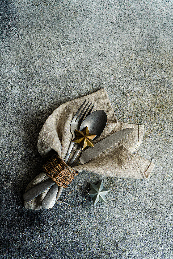 Draufsicht auf ein Vintage-Besteck mit Serviette, Löffel, Messer und Gabel auf einer grauen Fläche neben Weihnachtsschmuck bei Tageslicht