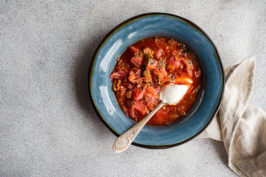 Top view of bowl with traditional Ukrainian soup borscht served in blue ceramic bowl on gray surface and white sour cream sauce