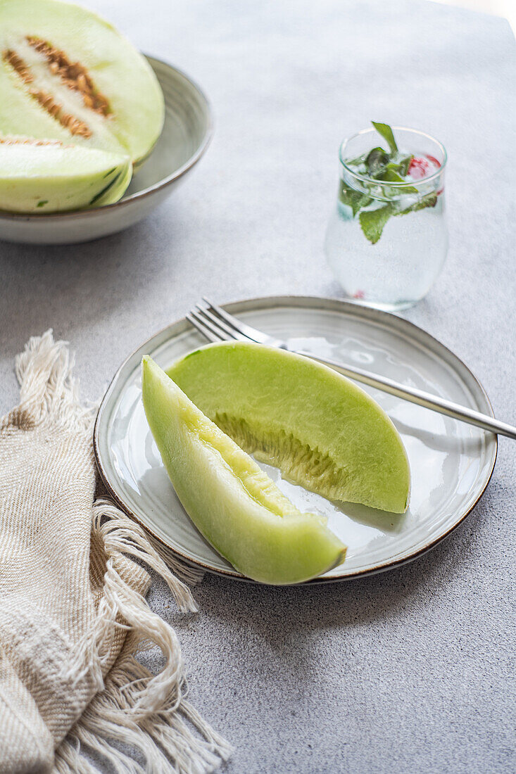 From above of green melon split in half placed in bowl and on plate with a lemonade on a concrete background