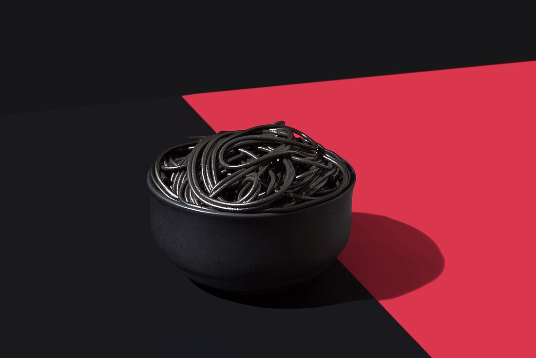 Black spaghetti in a bowl placed on black and red surface against black wall
