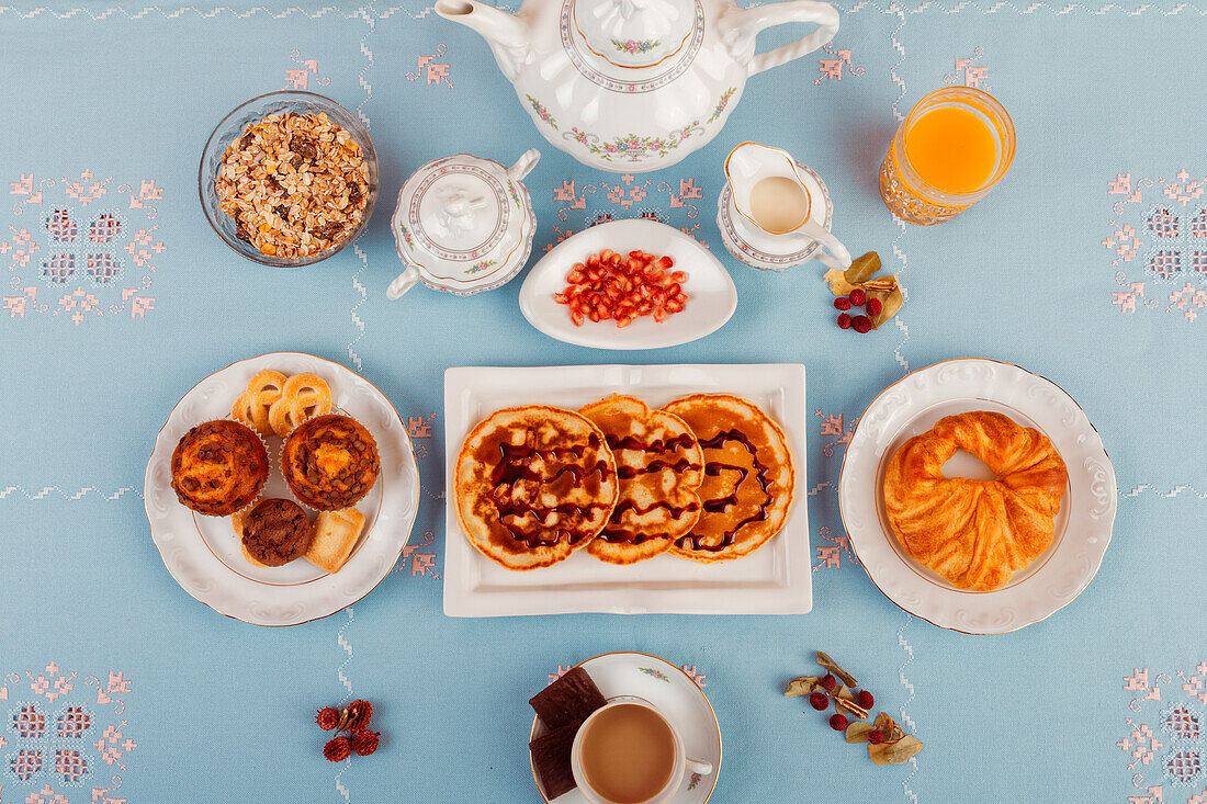 A top-view of a continental breakfast setup featuring pastries, cereal, fresh fruit, and beverages, laid out on a blue surface.