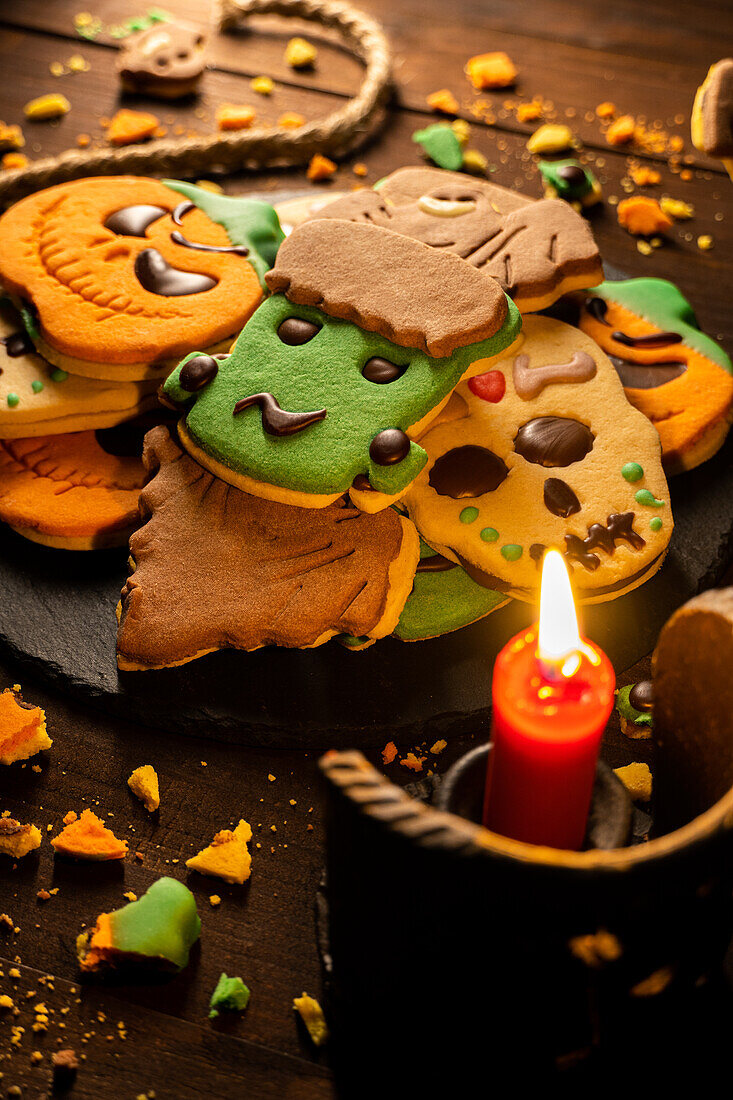 Draufsicht auf leckere Halloween-Kekse auf einem Teller auf einem Holztisch neben einem Seil mit einer brennenden Kerze