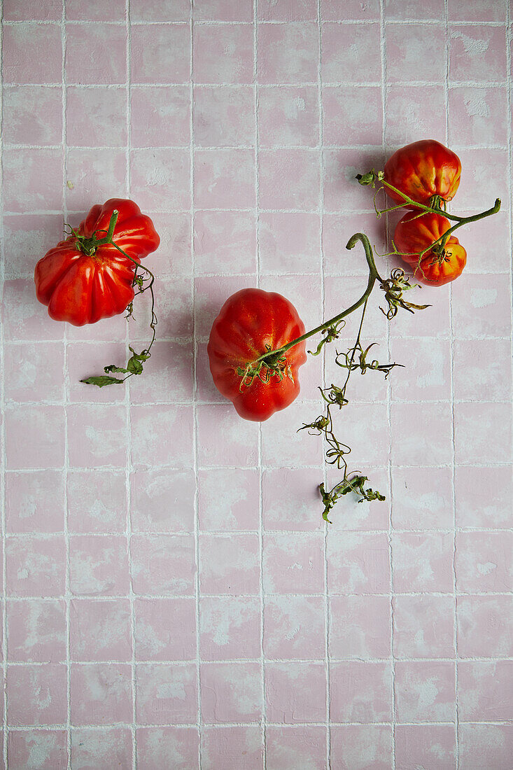 From above of fresh ripe beef tomatoes with stems and weathered leaves placed on tiled floor