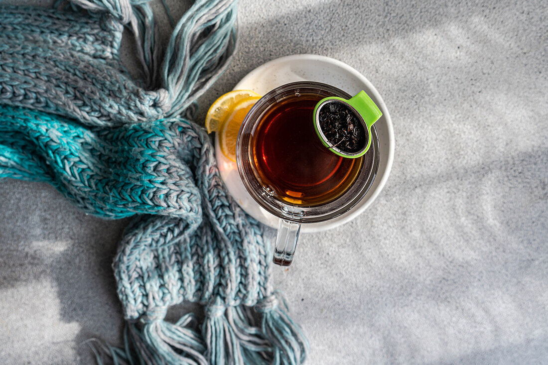 From above of cozy winter scene with a hot cup of tea and a lemon slice, accompanied by a soft, knitted scarf on a textured background