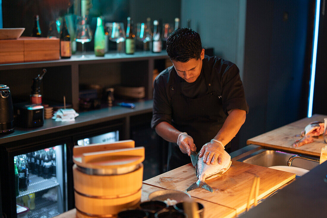 A skilled sushi chef carefully slices fresh fish in a sushi restaurant with a serene ambiance.