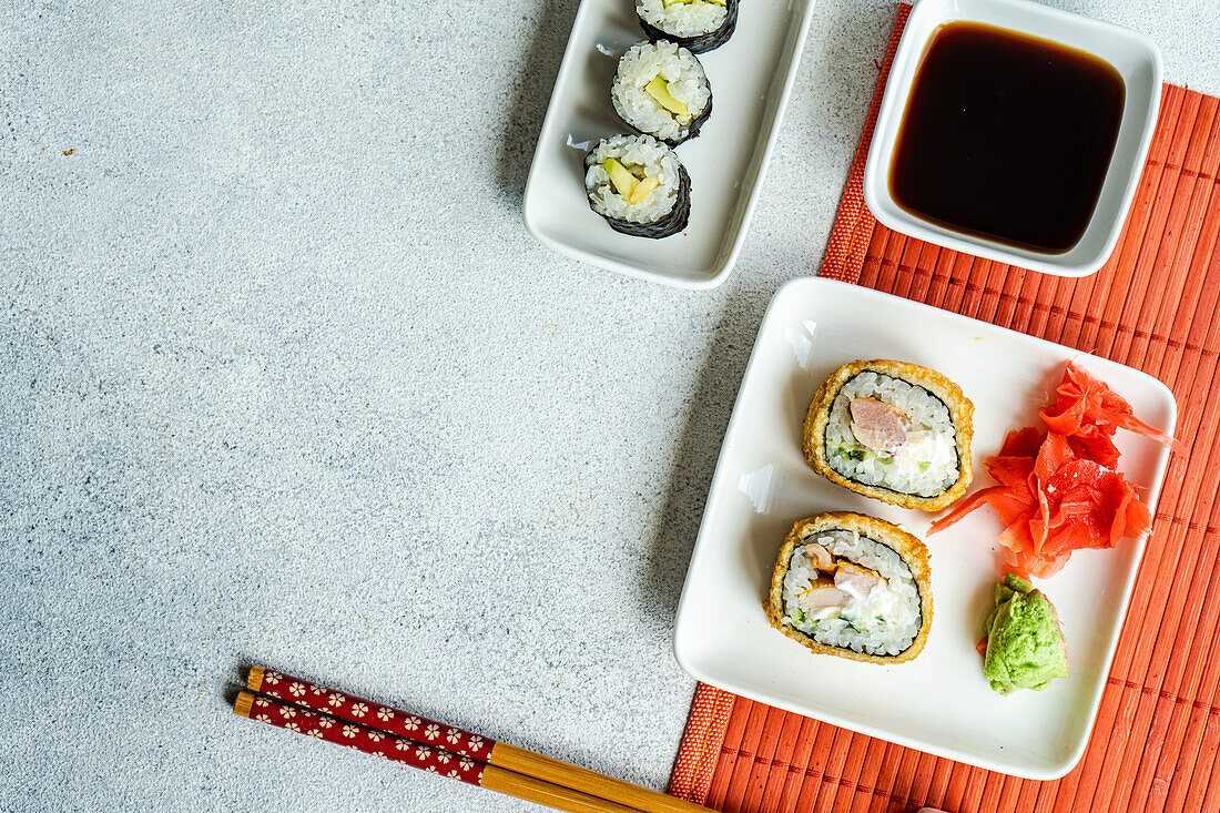 Verschiedene Sushi-Rollen auf Tellern mit Stäbchen und Sojasauce auf weißem Hintergrund von oben