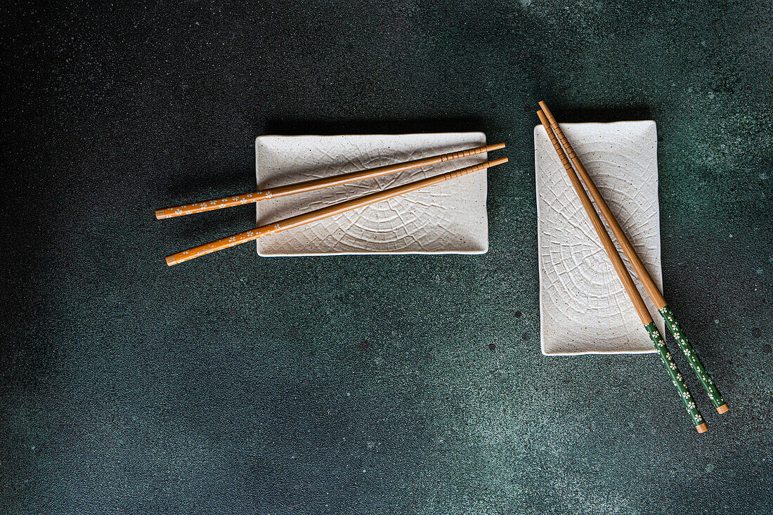 Blick von oben auf einen Satz weißer Keramikteller auf einem schwarzen Betontisch mit Stäbchen in einem asiatischen Restaurant