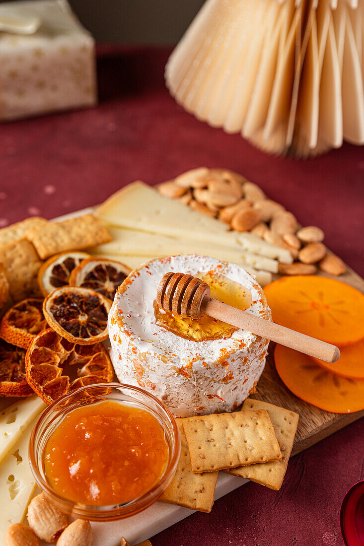 A sumptuous cheese board featuring a selection of fine cheeses, crackers, almonds, dried citrus slices, and a bowl of honey with a dipper.